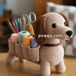 A crocheted dachshund-shaped organizer on a wooden table, holding various craft supplies such as scissors and yarn in its back pockets.