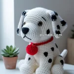 A crocheted Dalmatian toy with black spots and a red collar sits on a white table next to a small potted succulent plant.