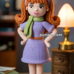 A crocheted doll with orange hair, wearing a purple dress, green scarf, and purple shoes, stands on a table with a lamp and books in the background.