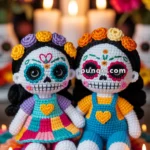 Two crocheted dolls inspired by Day of the Dead, featuring colorful clothing, floral headbands, and decorative face paint, seated on a vibrant knitted mat with candles and flowers in the background.