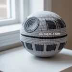 A crocheted Death Star replica placed on a white table by a window.