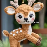 A hand holds a crocheted keychain in the shape of a cute deer with antlers and spotted fur.