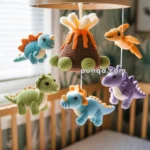 A baby's mobile hanging over a crib, featuring crocheted dinosaur figures and a volcano in various colors.
