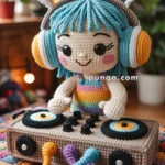A crocheted doll with blue hair wearing colorful headphones labeled "Groovy Tunes." The doll is posed as a DJ, with a smile, standing behind a crocheted DJ set, featuring turntables and colorful cords. The scene is set in a cozy room with soft lighting and houseplants in the background.