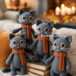 Four crocheted grey cats with orange scarves sitting on books and a fluffy blanket, in a cozy room with a lit fireplace in the background.