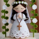 Crocheted doll of a girl in a white dress and veil, with a rosary and flowers, displayed on a round base labeled 'Prima Comunione Irene 08/08/2028.'