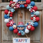 A decorative wreath for the 4th of July, featuring crochet figures and elements in red, white, and blue, with a central character wearing a top hat. Below hangs a sign reading 'HAPPY 4th of July.'