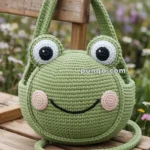A crocheted green frog-shaped bag with eyes and a smiling face, resting on a wooden bench in a garden setting.