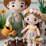 Crocheted dolls of a boy and a girl on a circular mat decorated with colorful flowers. The boy wears a brown hat, green overalls, and holds a yellow watering can. The girl wears a flower crown and pastel dress, carrying a basket with flowers.