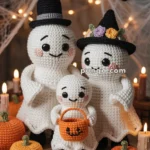 Three crocheted ghosts in Halloween costumes, with two adult ghosts wearing hats and a small ghost holding an orange pumpkin basket, surrounded by crocheted pumpkins and Halloween decorations, including webbing and candle-like accents.