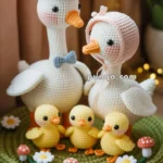 A crocheted family of geese and their ducklings, with the adult geese wearing hats, standing on a knitted green mat adorned with small flowers and mushrooms.