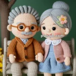 Two amigurumi dolls depicting an elderly couple sitting on a bench, with the man wearing glasses and a brown suit and the woman in a blue dress with a pink flower in her hair; they are holding hands under a tree in a garden setting.