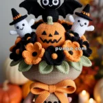 A crocheted Halloween-themed bouquet featuring a black bat, two white ghosts with witch hats, an orange jack-o'-lantern, and black and orange flowers, held together with a ribbon labeled 'BOO!'