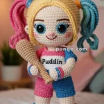 A crocheted Harley Quinn doll with colorful pigtails and a "Puddin" shirt, holding a bat, standing in a room with a plant and artwork in the background.