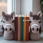 Two crocheted horse head bookends holding a row of books on a window ledge.