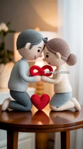 A crochet couple sits on a wooden table, kneeling face to face, holding a red infinity symbol between them.