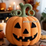 A crocheted pumpkin with a jack-o'-lantern face and green stem curls, surrounded by autumn leaves and candles in a festive setting.