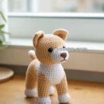 A crocheted dog figurine in beige and white yarn placed on a wooden table near a window.