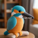 Crocheted bird with blue, orange, and white colors sitting on a wooden table in a cozy living room setting.
