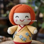 A handmade crocheted Kokeshi doll with reddish-orange hair, a smiling face, and wearing a yellow dress with blue embroidered flowers, sitting on a wooden stump outdoors.