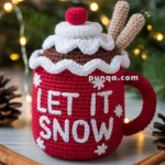 A crocheted red mug with the text 'LET IT SNOW' in white, decorated with a white trim, a red pom-pom, and two beige sticks, set on a festive background with pinecones and string lights.