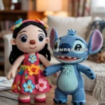 Two crocheted dolls, one resembling a girl in a colorful dress with floral patterns, and the other resembling a blue creature with large ears, both standing on a wooden table in a cozy living room setting.