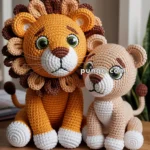 Two crocheted lion toys sitting on a wooden table, one large with a colorful mane and the other smaller with a plain beige body.