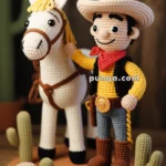 A crocheted figure of a sheriff, complete with a hat and badge, stands beside a white horse on a brown circular base adorned with crocheted cacti and rocks, with a "Sheriff" sign in front.