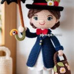 A crocheted doll dressed in a blue coat, white skirt, and black shoes, holding a black umbrella and a floral handbag, standing on a wooden shelf.