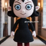 A handmade crochet doll with large blue eyes, black hair, and a black dress, standing in a hallway with arched windows and lit wall sconces. The doll also wears red and black striped stockings and red shoes.