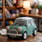 A crocheted model of a classic mini cooper car, in green with white roof and detailing, placed on a wooden table in a cozy room with yarn and books on shelves in the background.