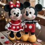 Crocheted dolls resembling classic cartoon characters, dressed in red outfits with white polka dots, standing on a wooden table surrounded by heart-shaped decorations and the word 'LOVE' spelled out with wooden letters.
