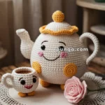 A crocheted teapot and teacup with smiling faces and yellow accents, placed on a crocheted doily with a pink rose beside them.