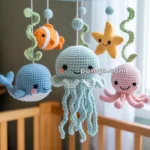 A crocheted baby mobile featuring a smiling jellyfish, octopus, clownfish, whale, and starfish hanging above a crib.