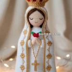 Crocheted figurine of a person with a crown, holding a red heart, wearing a white robe with gold trim and floral patterns, and a rosary hanging from their hands.