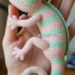 A handmade macramé chameleon figurine with pink and green stripes, held in the palm of a person's hand.
