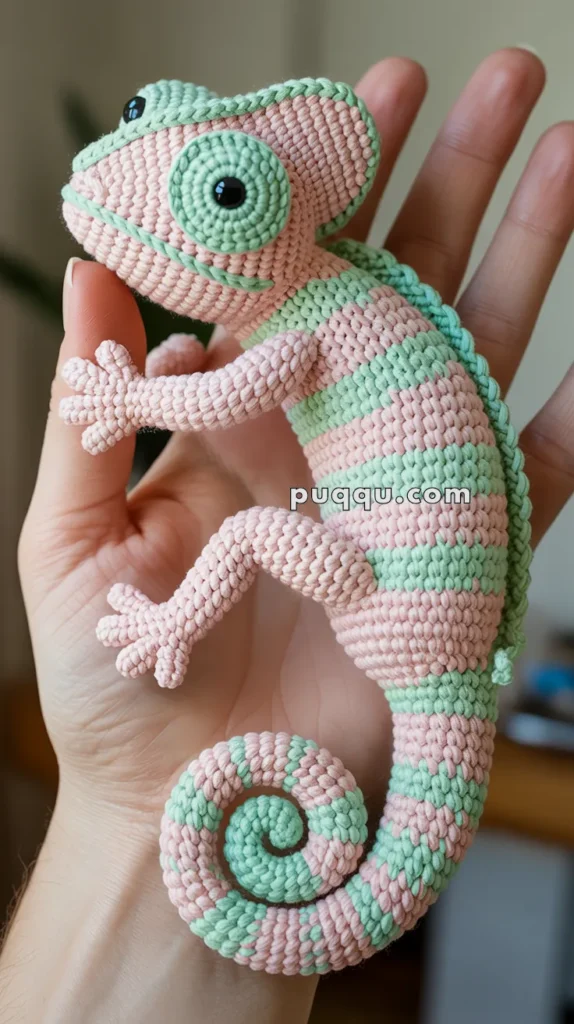 A handmade macramé chameleon figurine with pink and green stripes, held in the palm of a person's hand.