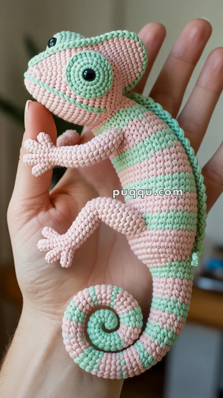 A handmade macramé chameleon figurine with pink and green stripes, held in the palm of a person's hand.