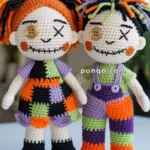 Two crocheted dolls with playful, mismatched outfits in Halloween colors; one doll with orange and black hair, a button eye, and a patchwork dress, and the other with multicolored hair, button eyes, and striped overalls, standing side by side on a table.
