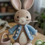 A crocheted rabbit toy wearing a blue jacket is placed on a wooden table, accompanied by crocheted carrots and cabbages, next to a small basket.