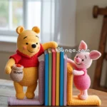 Crocheted figures resembling a bear and a pig holding a stack of colorful books upright on a wooden table.