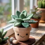 A crocheted succulent plant in a smiling pot placed on a wooden windowsill, with sunlight streaming through the window.
