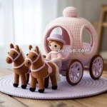 A handmade crocheted scene featuring a pink carriage with windows, driven by a doll wearing a pink hat and dress, pulled by two brown horses with pink harnesses, all placed on a wooden table.
