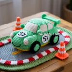 A crocheted toy set featuring a green car with "57" on it, placed on a knitted racetrack mat, accompanied by small crochet traffic cones, all displayed on a wooden surface.