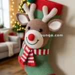 A crocheted Christmas stocking shaped like a reindeer with a red nose, brown face, and striped scarf, hanging on a wall decorated with garlands and lights.