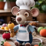 A crocheted rat doll wearing a chef's hat and apron, holding a crocheted drumstick, with various crocheted vegetables like carrots and tomatoes nearby, set on a wooden table.