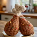 Two crocheted chicken drumsticks on a plate, with colorful stitching resembling sprinkles, sitting on a wooden table.