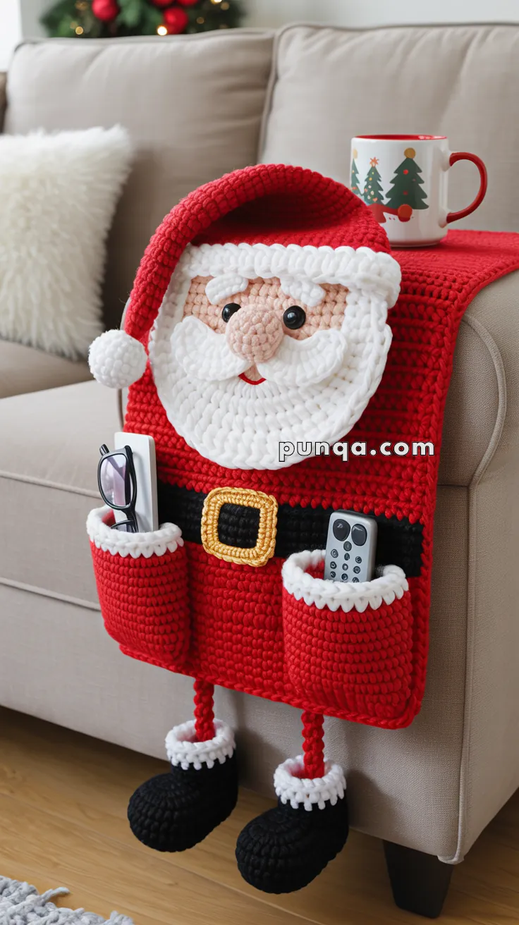 A crocheted Santa-themed armchair organizer with a Santa face and hat, featuring pockets holding a remote and eyeglasses. It hangs over the arm of a beige sofa, accented with a decorative holiday mug on the armrest.