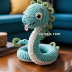 A crocheted sea serpent toy with blue and white yarn, green spikes, and large eyes sitting on a wooden coffee table in a living room setting.