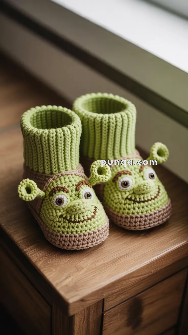 A pair of green knitted slippers featuring a character with a friendly face and ears, placed on a wooden surface next to a window.